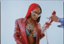 Sexyy Red poses with a red chorded phone on a light blue studio background 