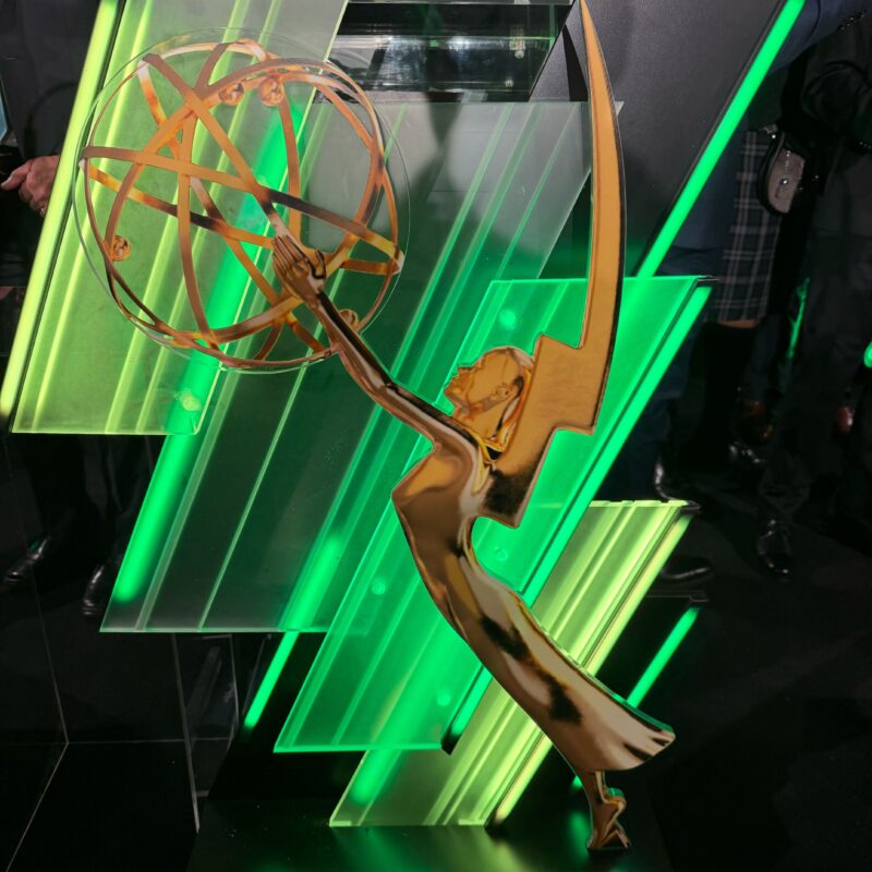 Gold Emmy-style statuette in front of green illuminated panels at an award ceremony podium.