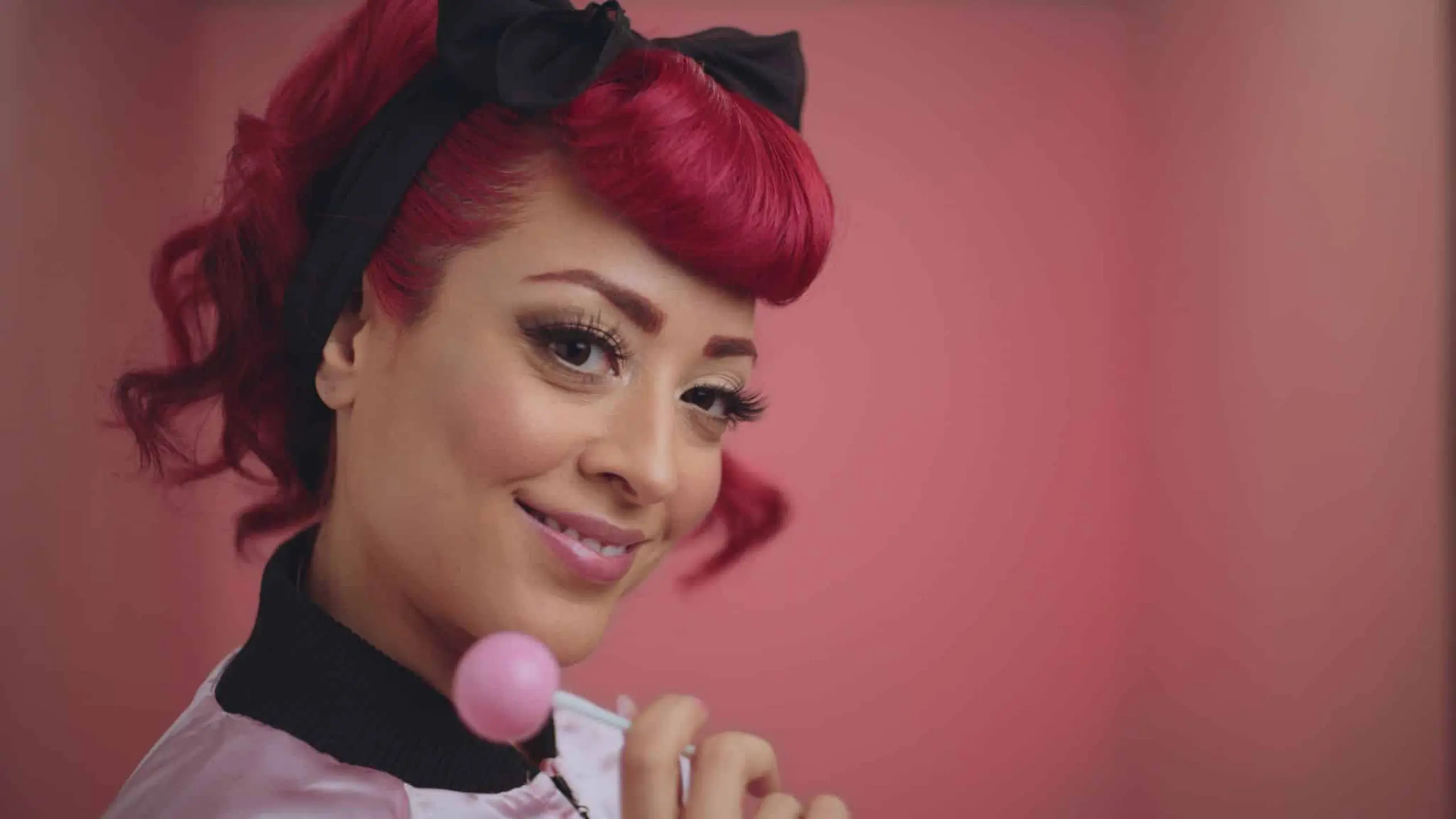 Pretty Vulgar 20 Marielle with red hair posing for the camera smiling with a pink lollypop