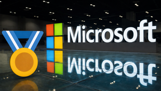 Bold Microsoft logo with vibrant colors and a gold medal icon on the left, reflecting on a glossy floor. The scene conveys achievement and innovation.