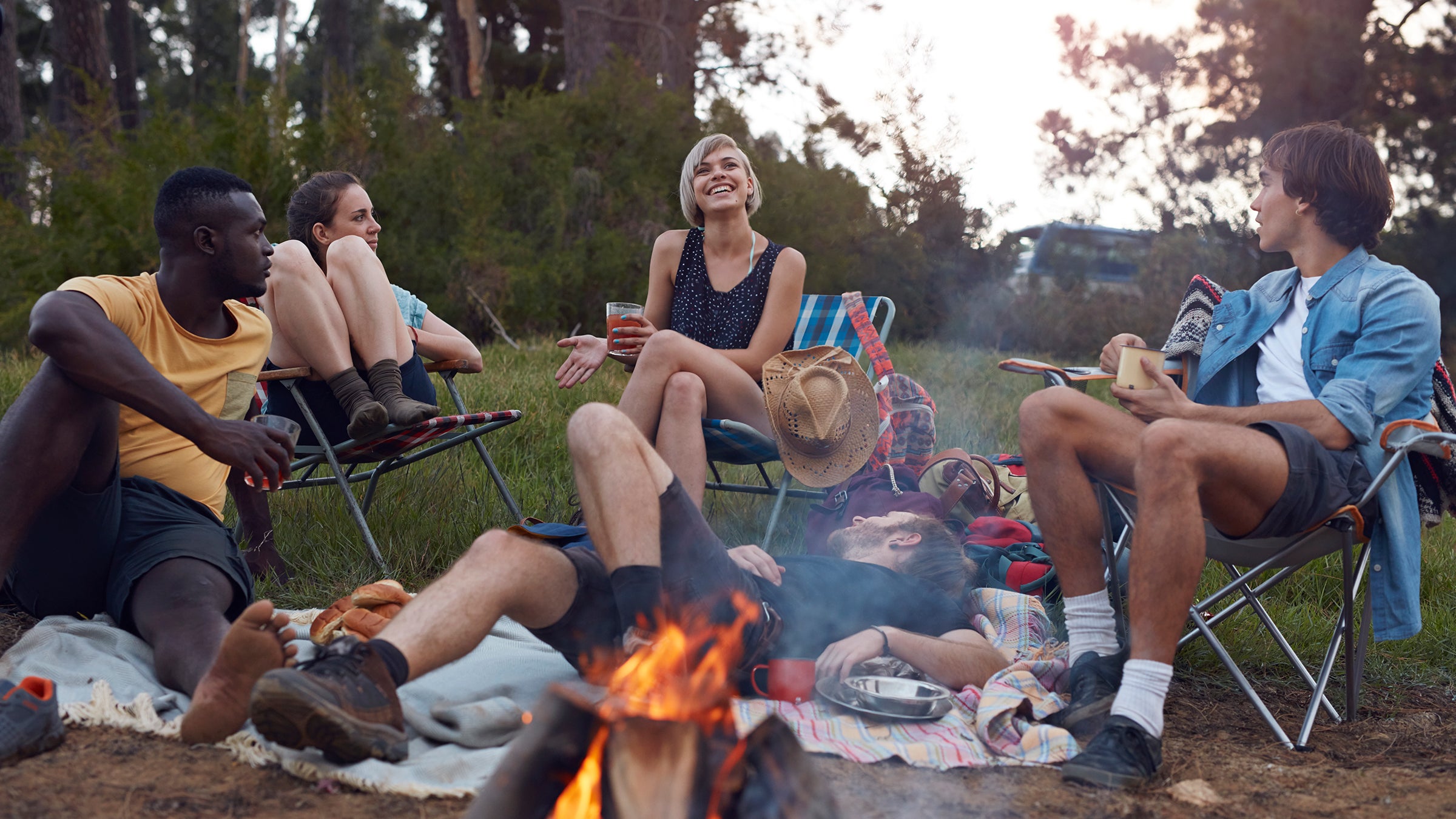 Group of friends on camping trip, by the lake with tent and making bonfire