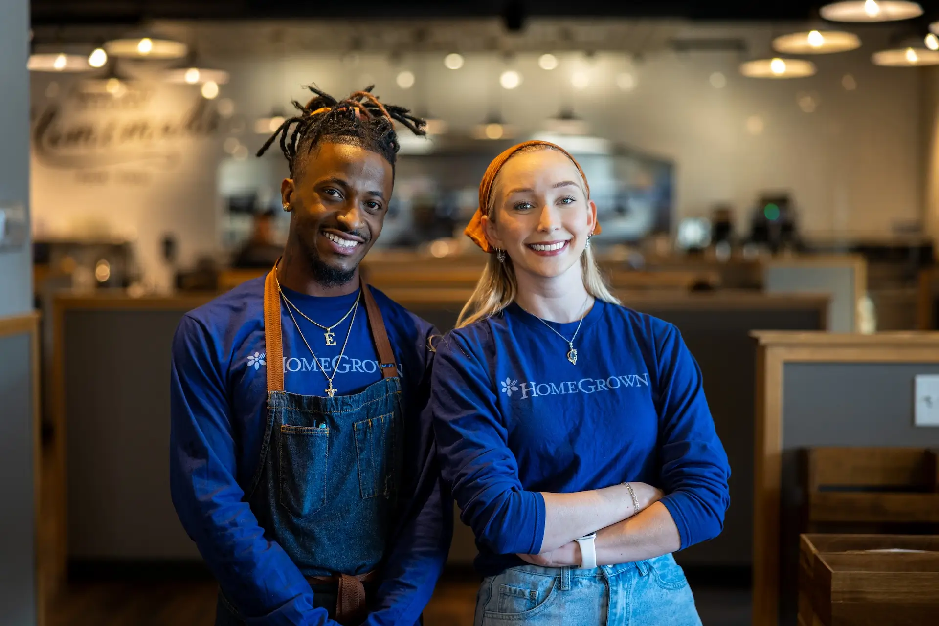 Two smiling HomeGrown employees wearing blue shirts standing inside a restaurant.