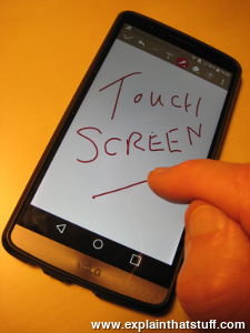 Writing the words 'touch screen' in red ink on a handheld smartphone touchscreen.