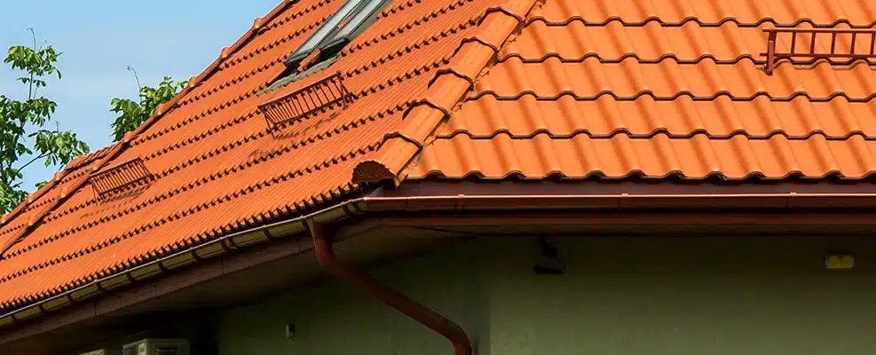 Orange tiled roof featuring attic windows and chimneys. Conifer Gutter Services offers reliable gutter solutions for homes with unique roof designs.