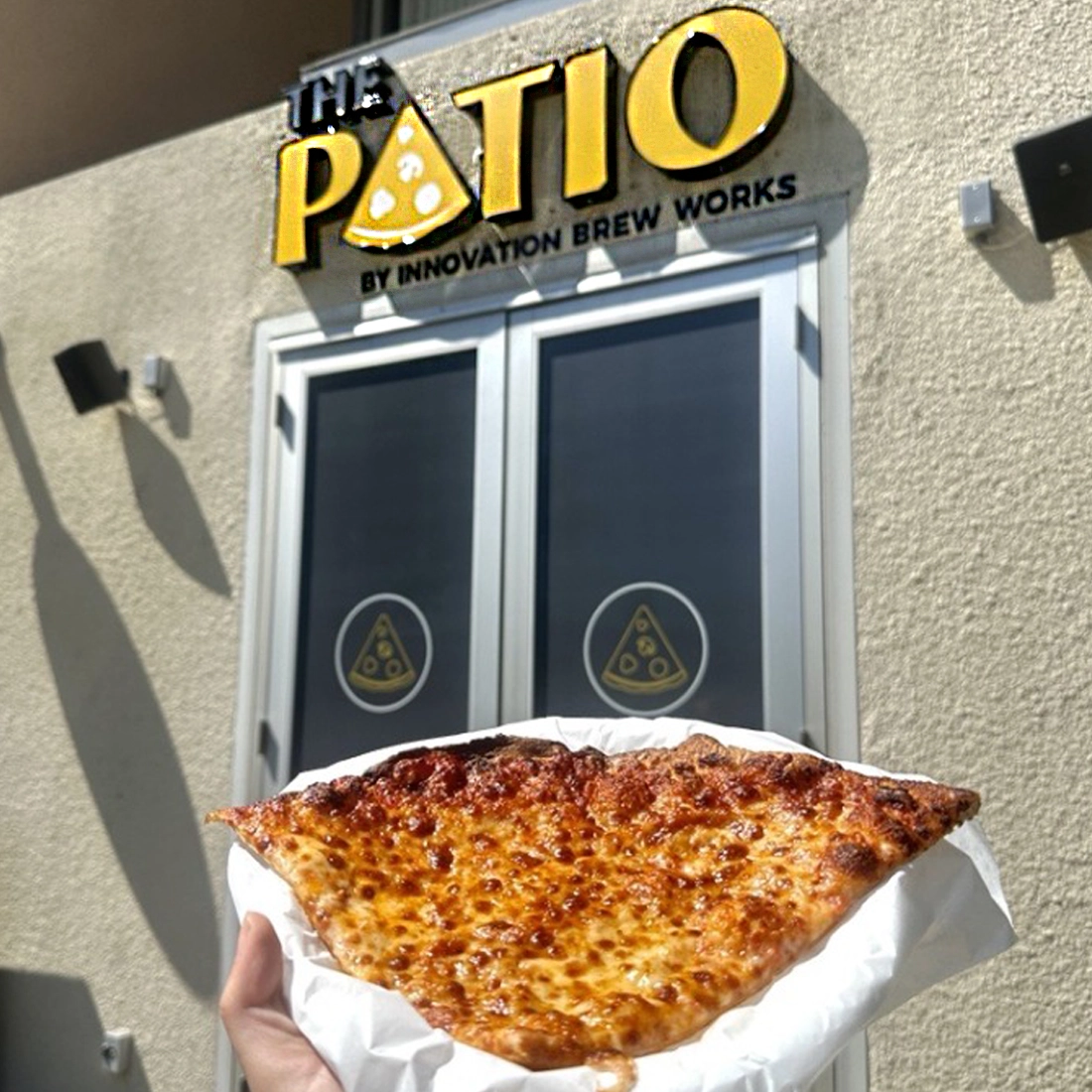 patio-square The Patio by Innovation Brew Works store front. a person has pizza slice in their hand