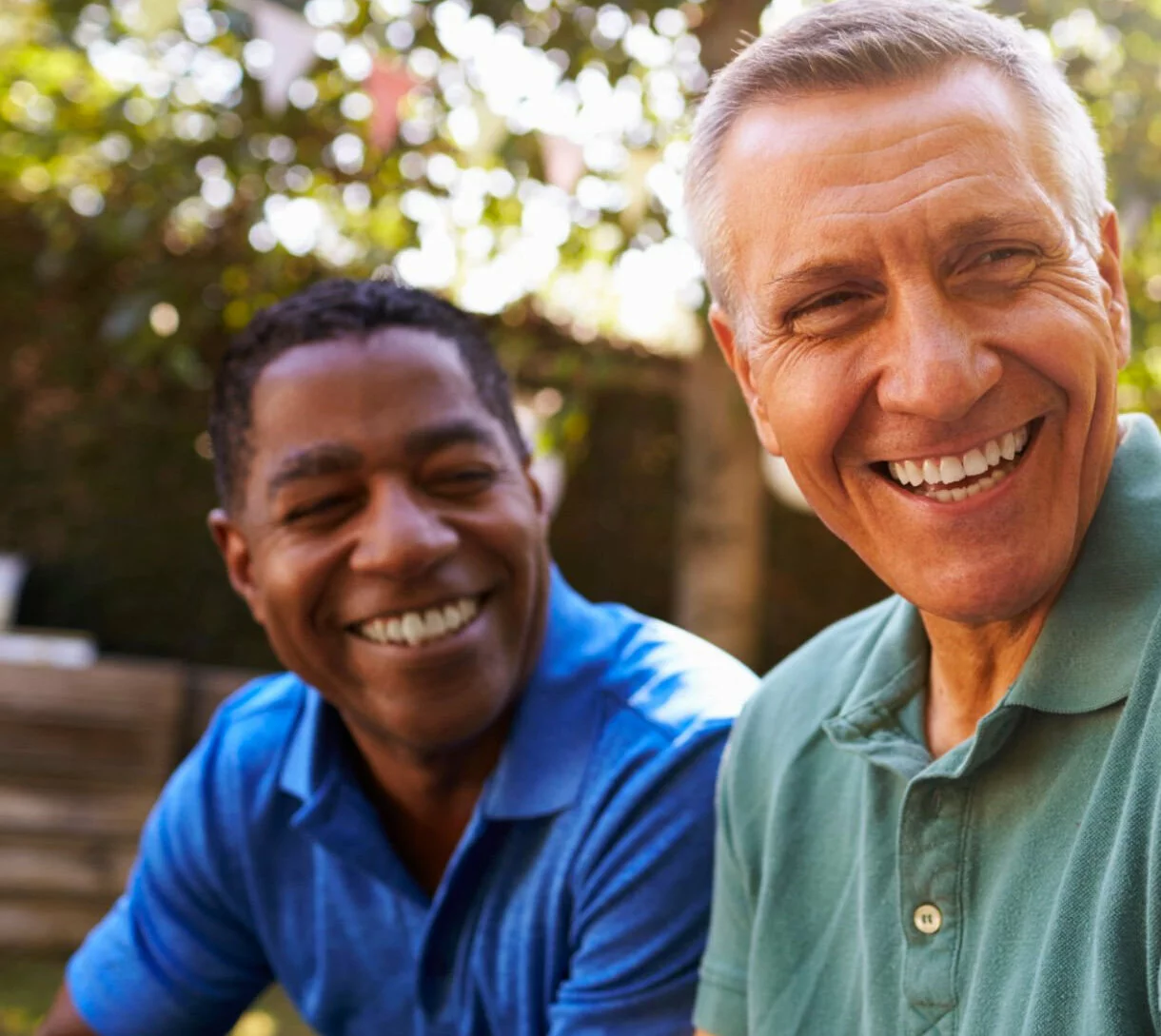 caucasian man and black man smiling together outside on a sunny day.