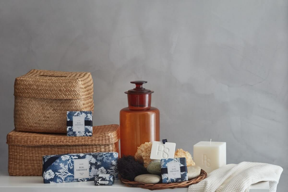 A decorative arrangement featuring woven baskets, an amber glass jar, candles, and various natural sponges and stones on a neutral background.