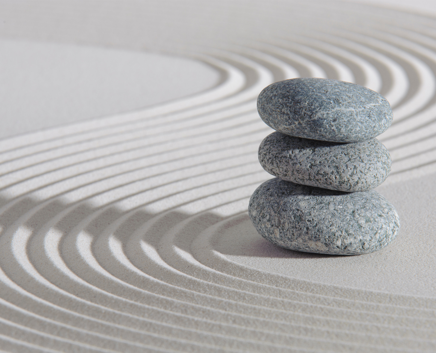 Three stacked gray stones on a textured sandy surface with curved lines creating a harmonious background.