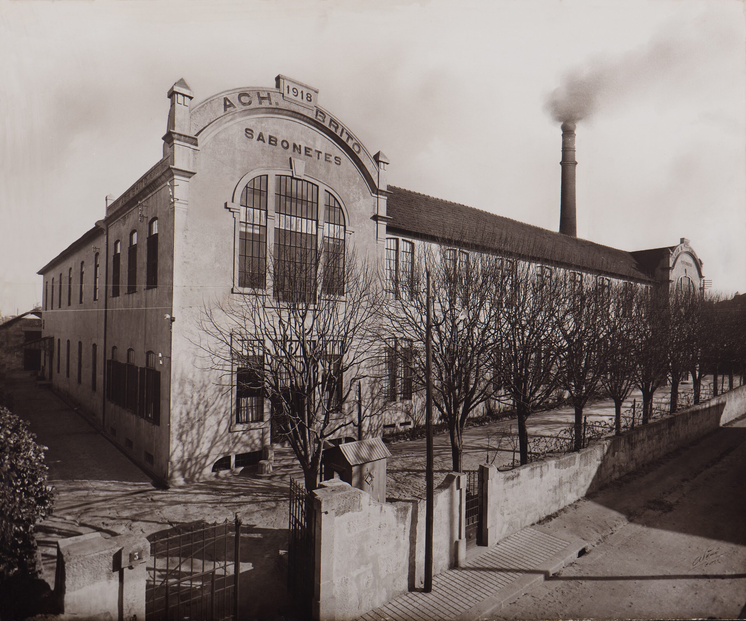 歷史悠久的工廠建築,外牆標示著1918年,高聳的煙囪正噴吐著煙霧,周遭環繞著光禿禿的樹木。