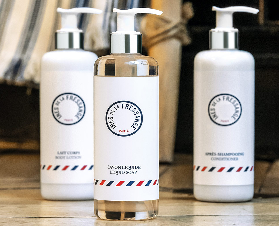 Three bottles of personal care products are displayed: a liquid soap, a conditioner, and a body lotion, each labeled with simple, stylish designs featuring a round logo and classic typography.