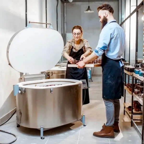 Two people standing in front of a large metal kiln.