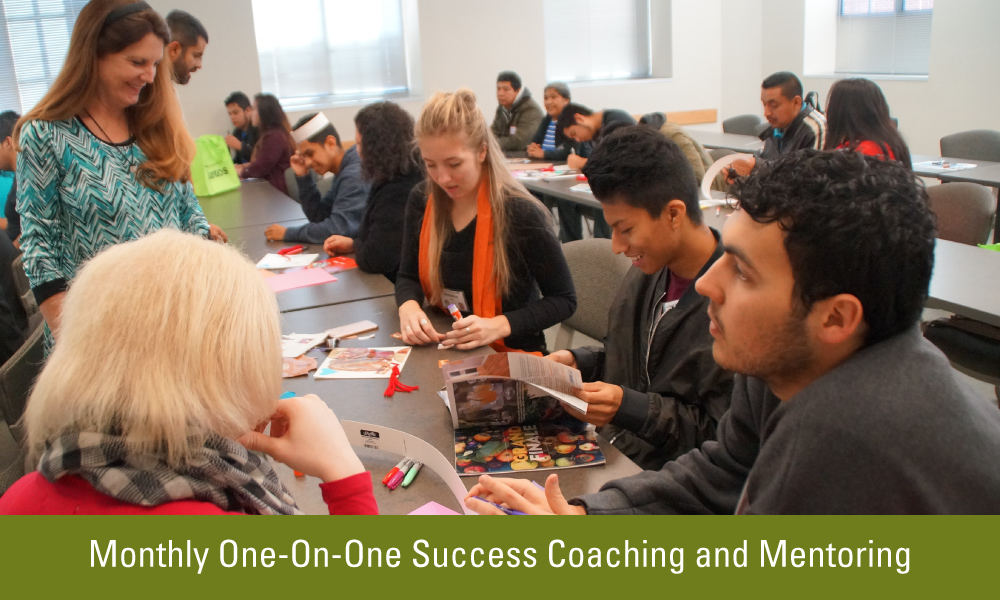 a group of students and parents are sitting at tables while two facilitators, one male and one female, walk around and check in on their progress.