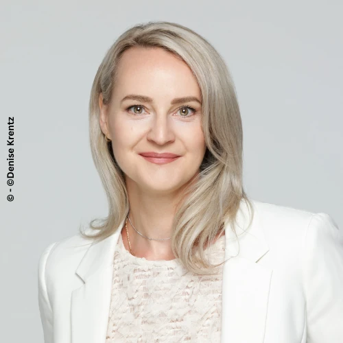 Mirja Rousselle mit einem wei&szlig;en blazer einer weu&szlig;en bluse und blondem haar mit eine hellgrauen hintergrund