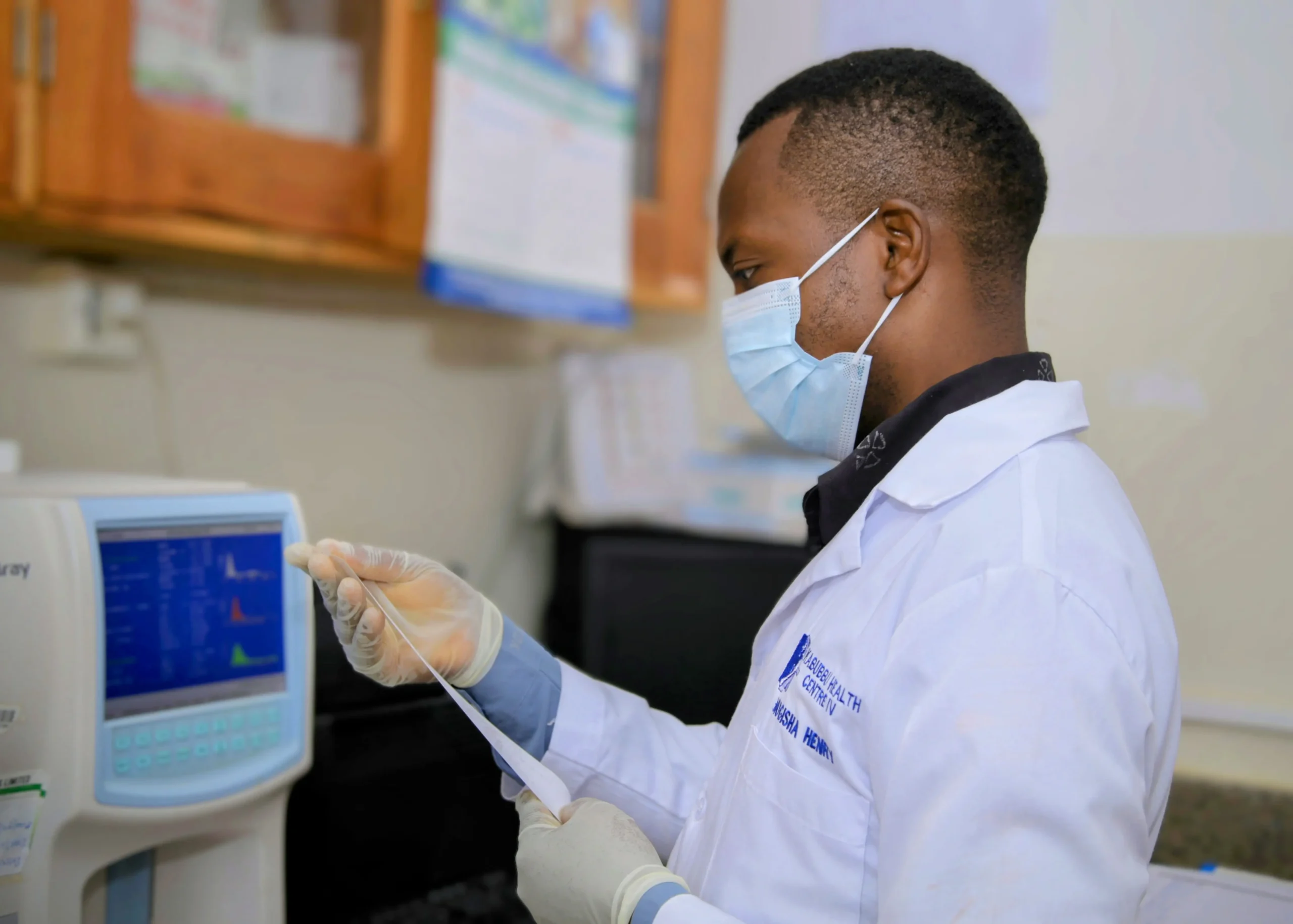 Lab technician at Kabubbu Health Center IV reviewing results from a blood testing machine
