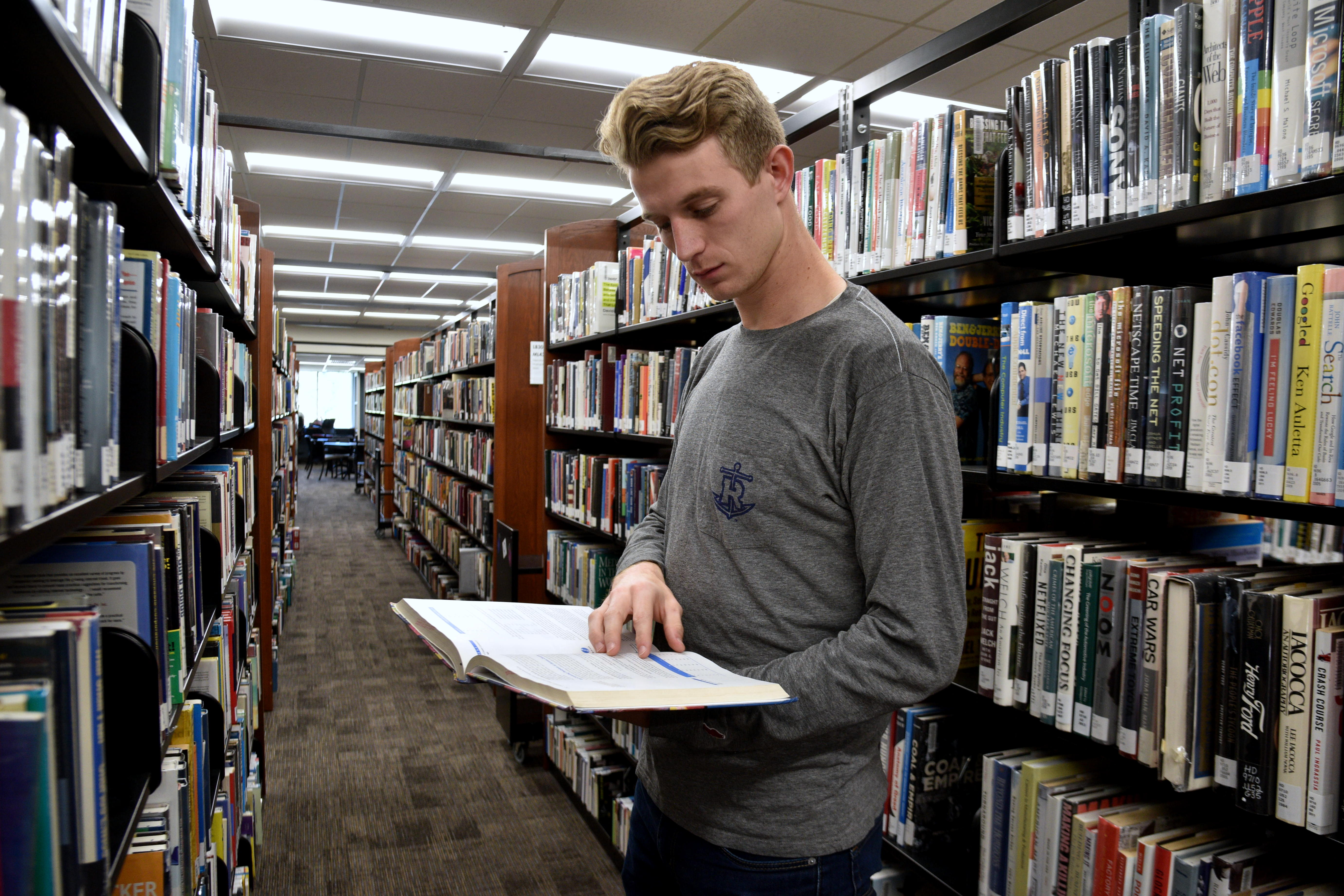 student viewing a book in the library stacks