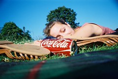 Young brunette woman sunbathing in Hampstead Heath, London, eyes closed, with sandals and a Coca-Cola can placed in front of her face.