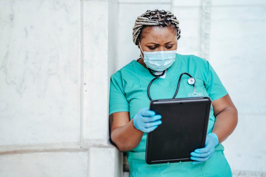 health care worker wearing a mask standing against a wall looking at a medical chart