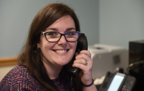 woman with brunette hair and eyeglasses smiling while answering telephone