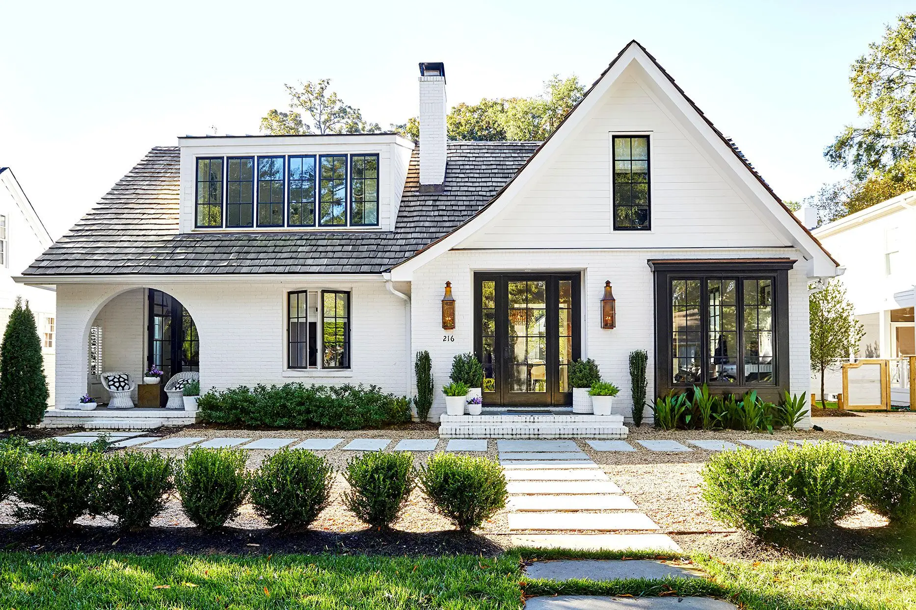 Charming white house with black trim, lush lawn, and stone path.