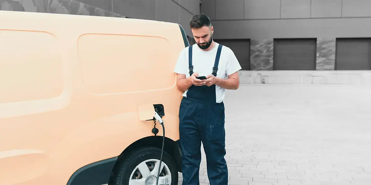 A driver charges an electric delivery van outside a depot