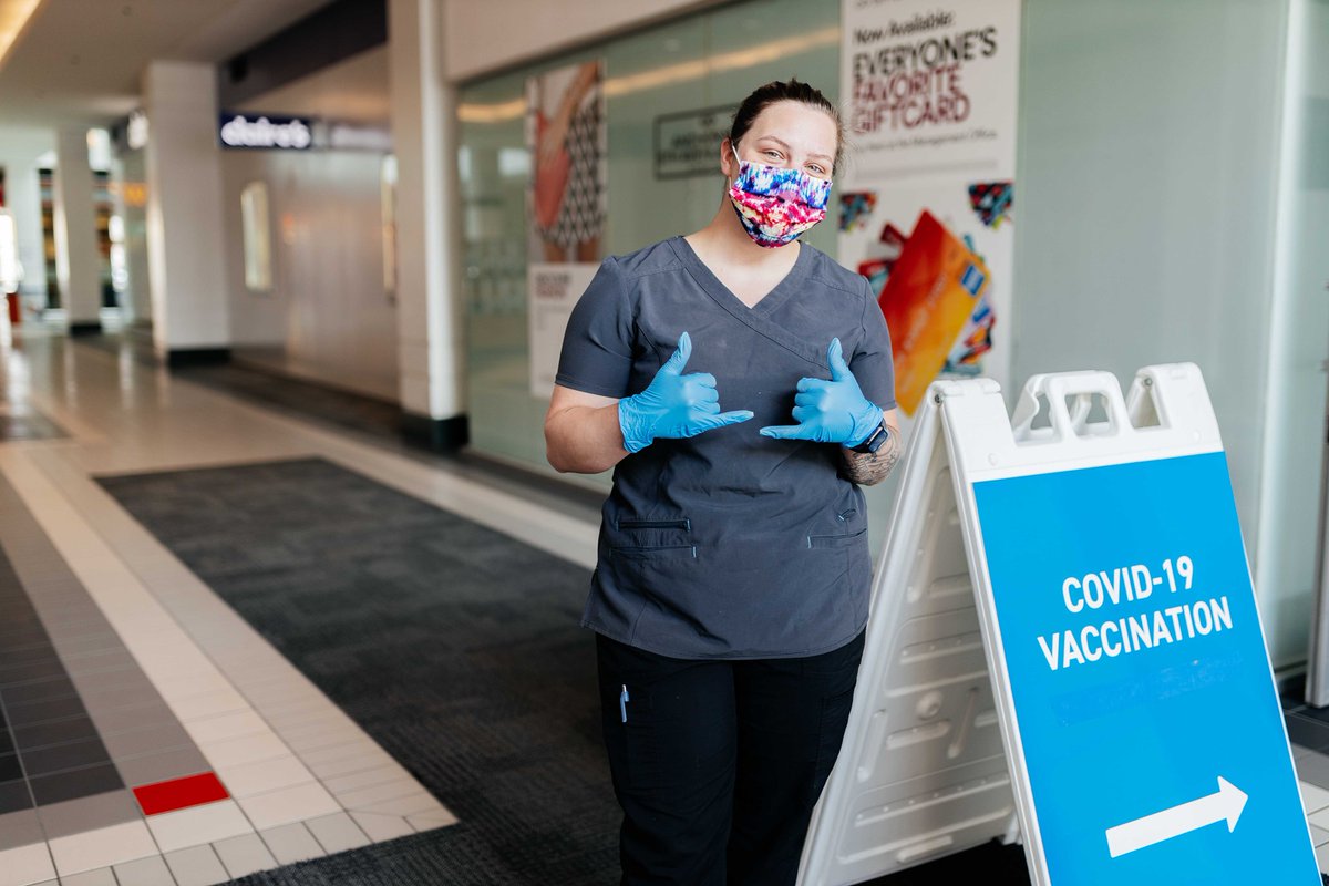 A health care worker stands next to a COVID-19 vaccination sign