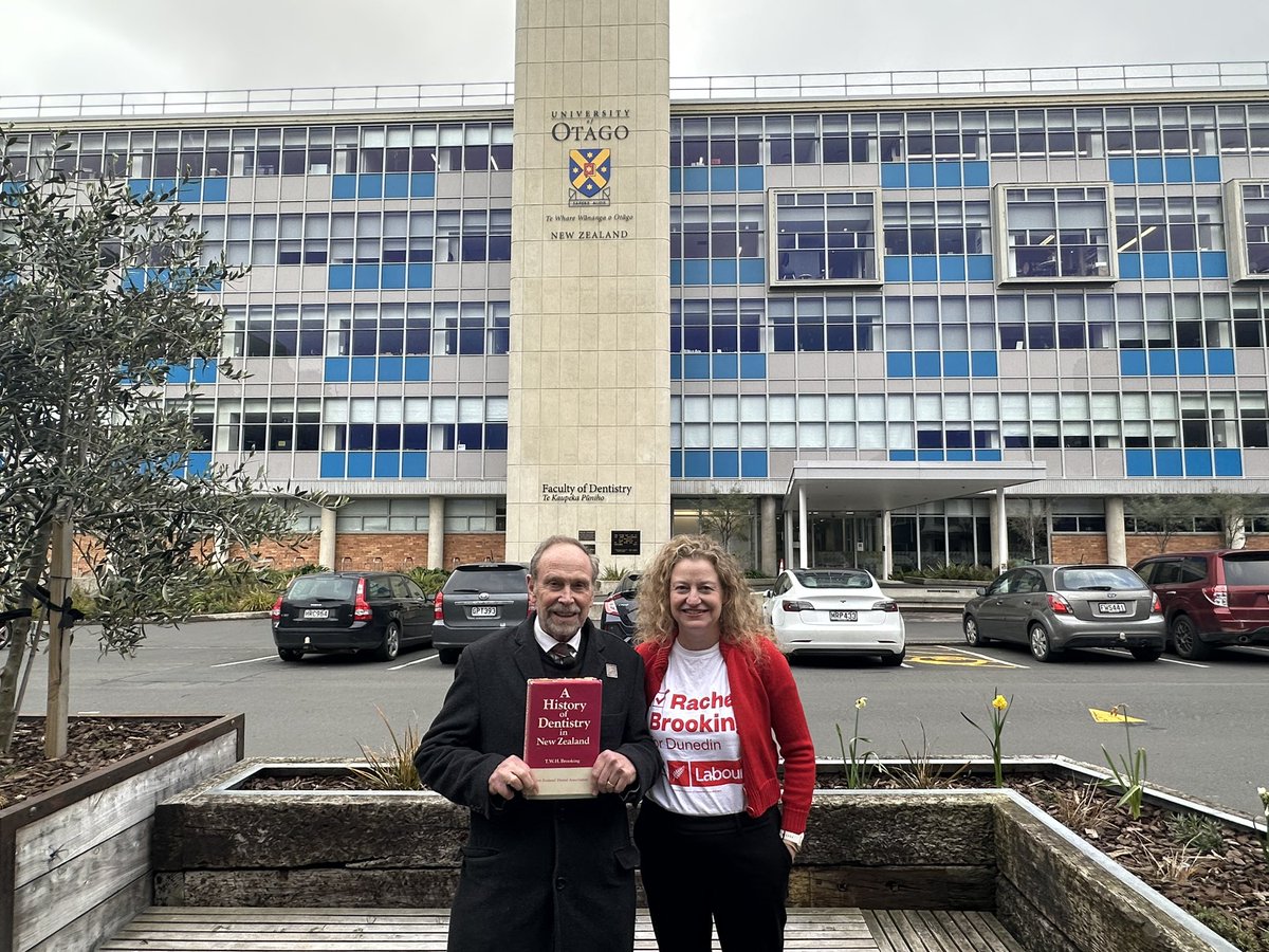 Rachel and her dad standing outside the University of Otago Dental School whilst holding the book ‘A History of Dentistry in New Zealand’.