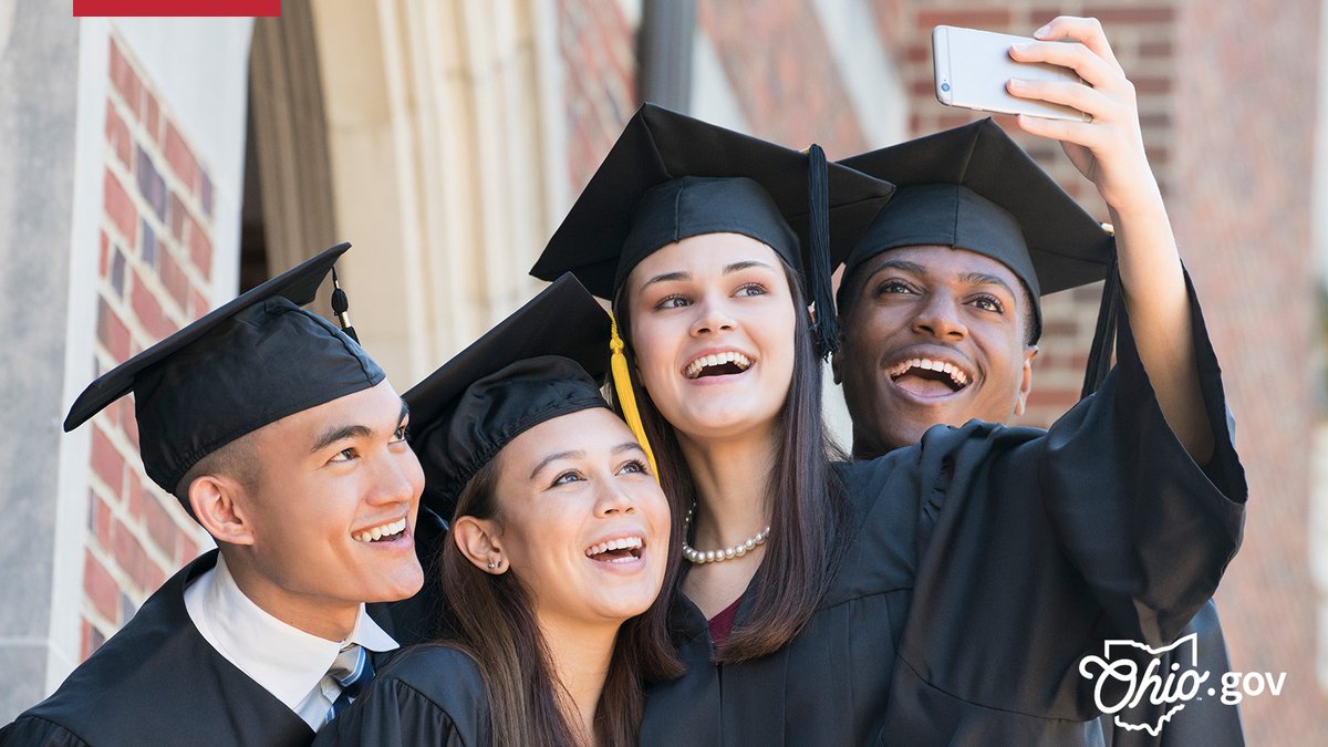 A diverse group of high school graduates smile and pose for a group selfie.