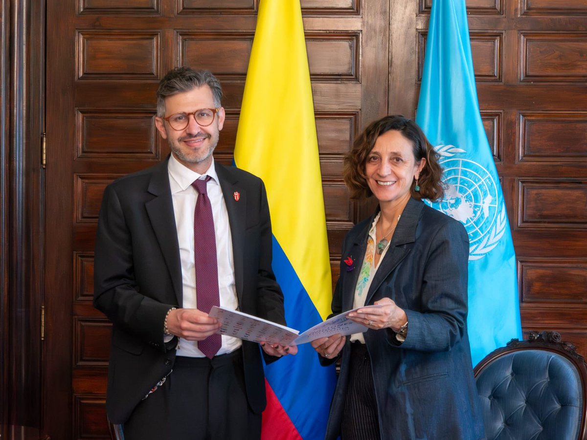 Coordinadora Residente de Naciones Unidas junto al viceministro de multilaterales de la Cancillería de Colombia en presentación protocolar posan de pie frente a las banderas de Colombia y de Naciones Unidas.