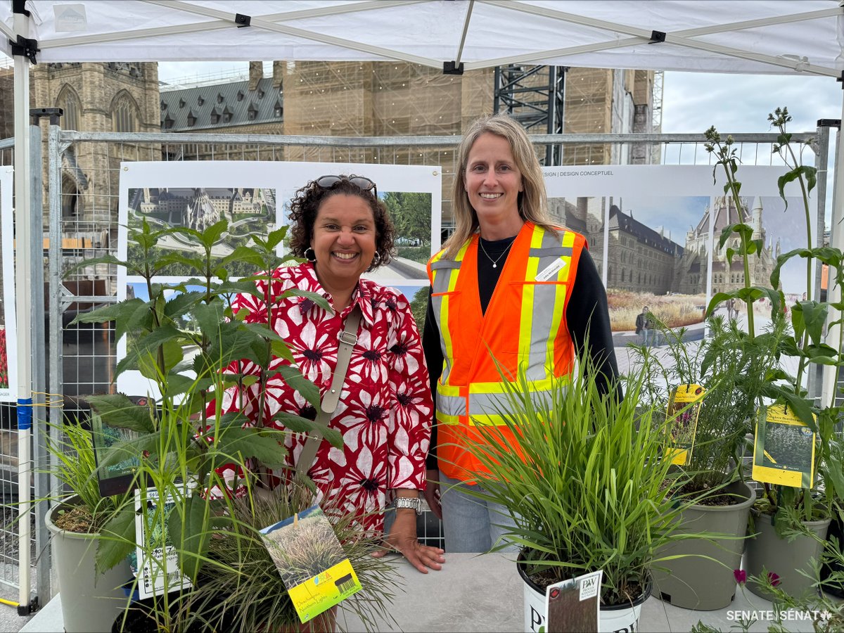 Senator Bernadette Clement stands beside a woman wearing a safety vest behind a table displaying a variety of plants and greenery.