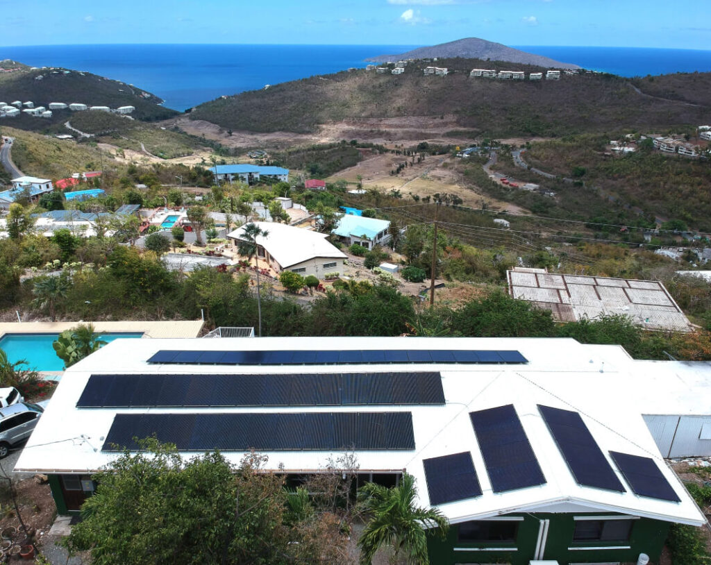 Solar panels installed on a residential roof overlooking a scenic view of hills and ocean, highlighting sustainable energy solutions in the Caribbean.
