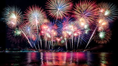 Colorful red, white, blue and gold fireworks burst over the water at night.