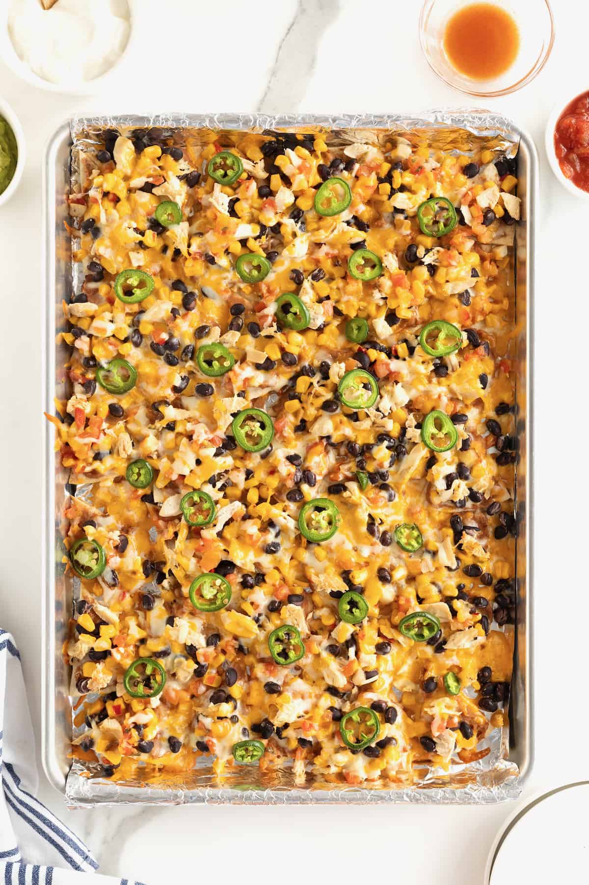 An aluminum sheet pan filled with nachos topped with cheese, black beans and jalapeรฑo slices.