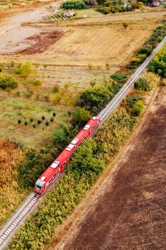 Red passenger train traveling through countryside, aerial view