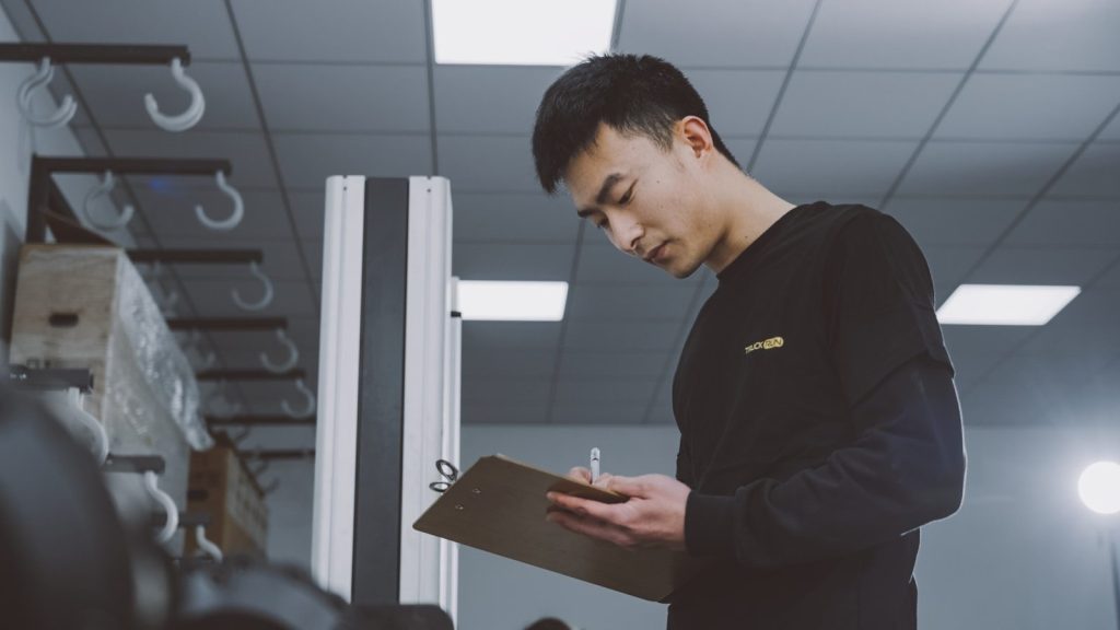 a man standing in a room holding a clipboard; product quality
