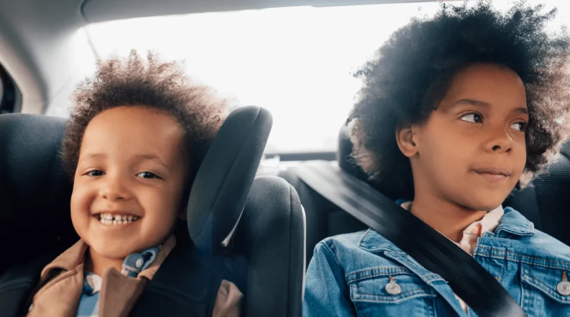 A girl sits beside her younger sister in the back seat of a car.